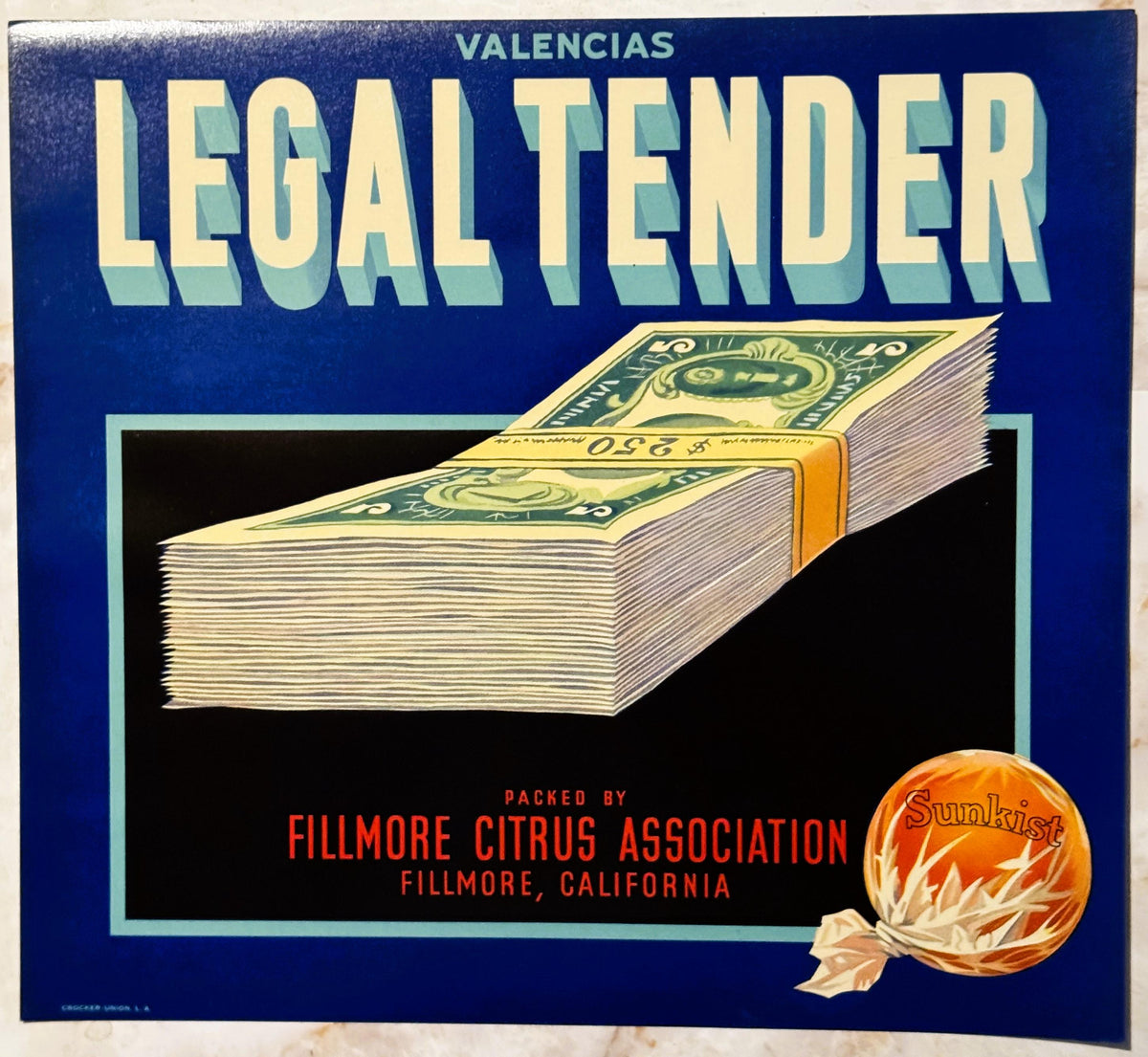 Vintage fruit crate label with dark blue background showing a stack of paper currency tied with gold band, orange fruit with 