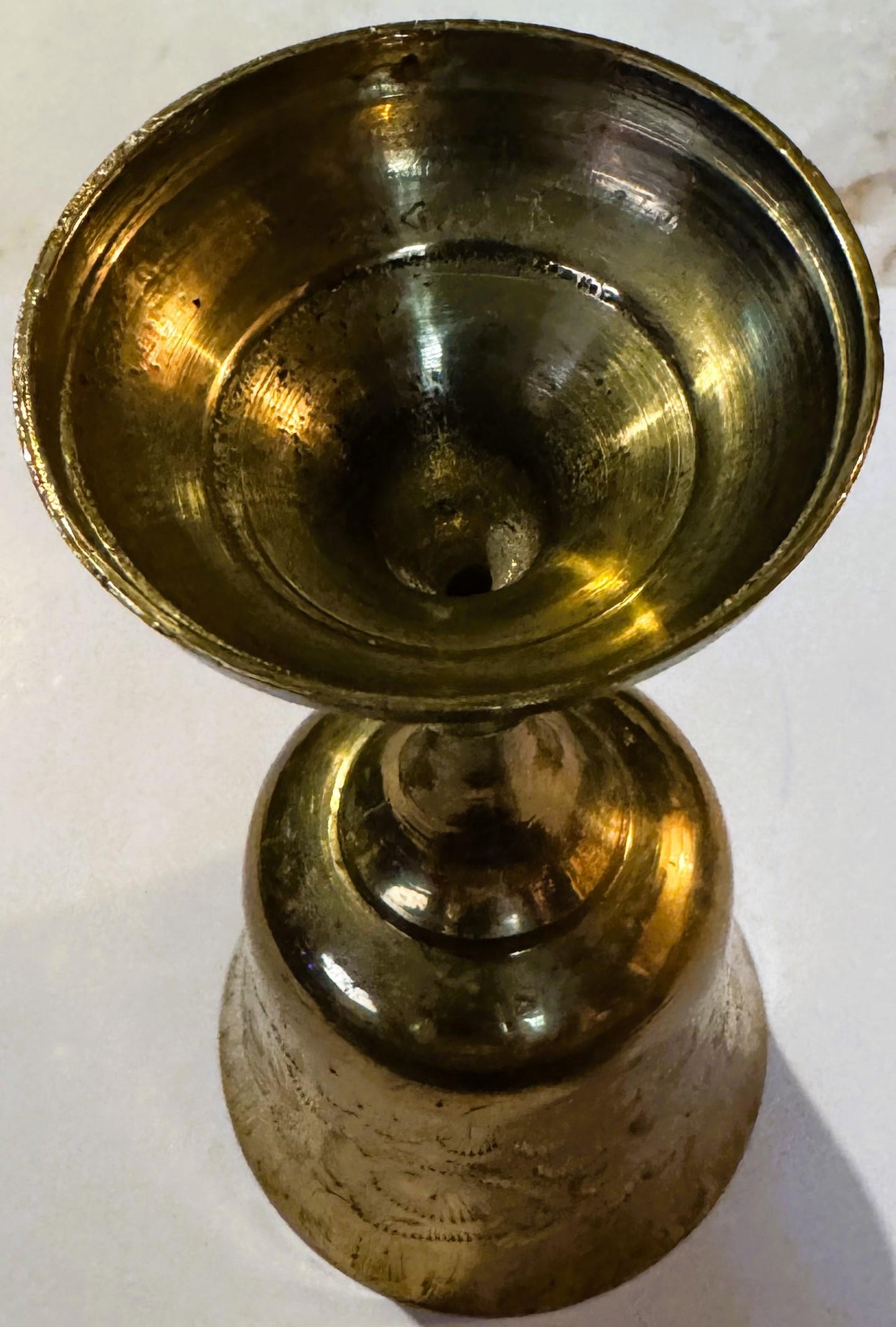 Brass goblet with etched bright-cut engraving on pedestal base, shown from above against white background, displaying patina 