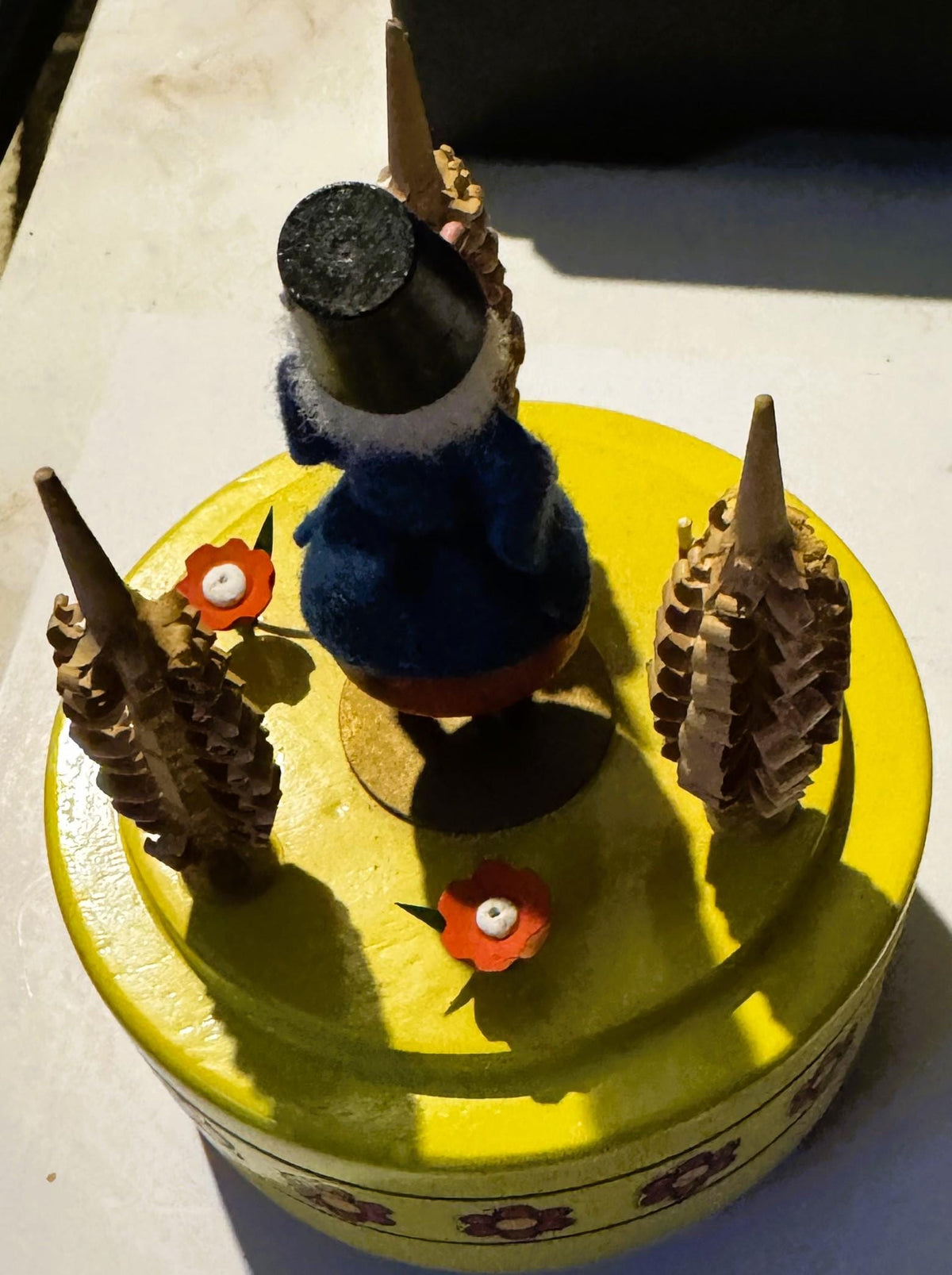 Vintage music box with yellow base featuring blue felt dancing figure with cone hat, brown pinecone arms, and small red flowe