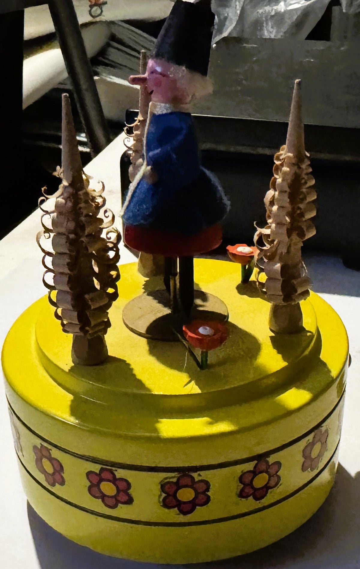 Vintage yellow music box with red flower band and wooden carved spires, wooden folk figure in blue dress and pink head rotati
