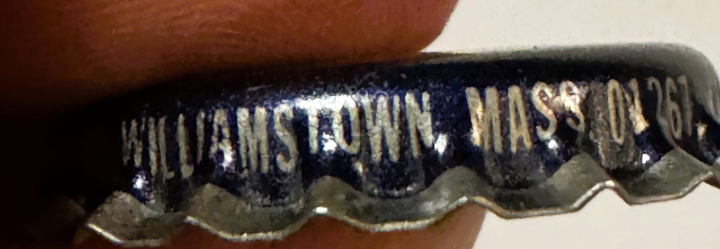 Close-up of vintage bottle cap with dark blue and gold embossed text reading "WILLIAMSTOWN MASS" held by a person's finger fo