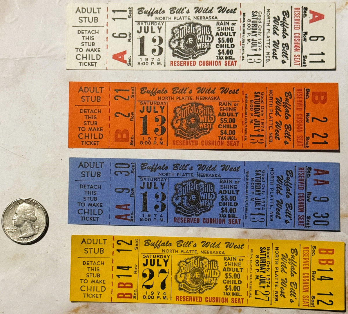 Four vintage 1974 Buffalo Bill's Wild West show tickets in tan, orange, blue, and yellow with a quarter for scale