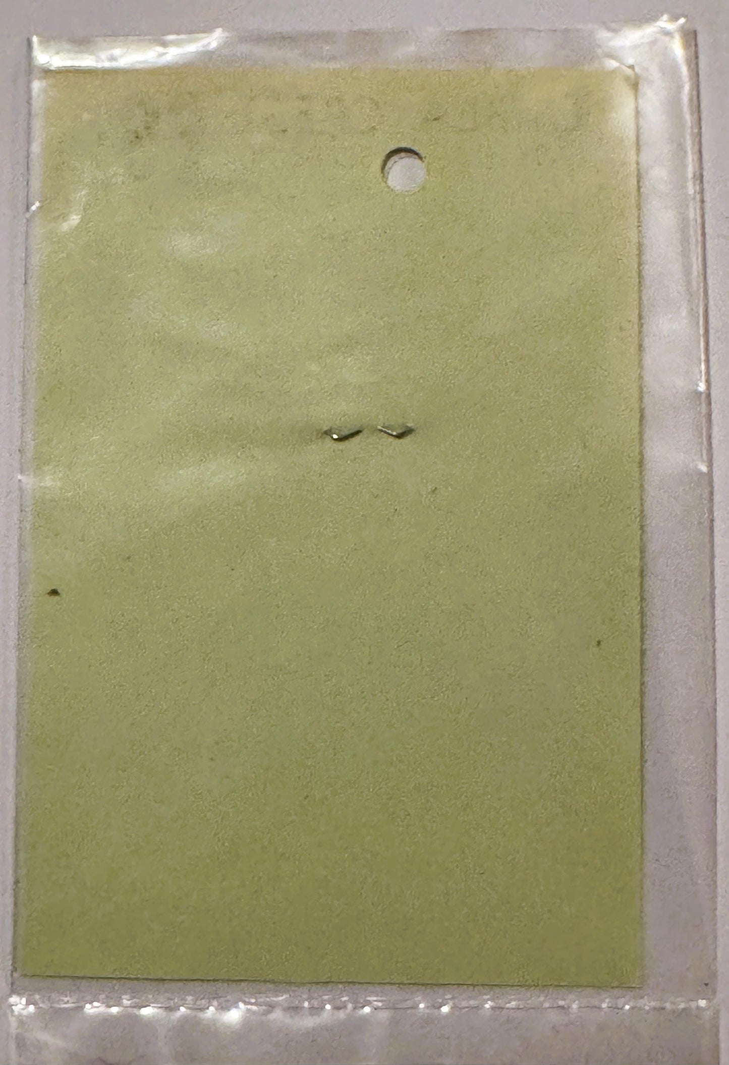 Pale yellow-green rectangular decal sheet in clear plastic packaging, showing two small slits in center, mounted on white bac