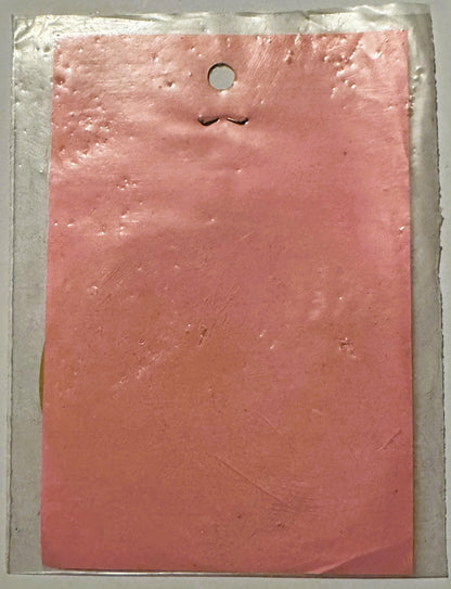 Pink rectangular decal with closed eyes and small mouth on white backing card, hole punched at top for display