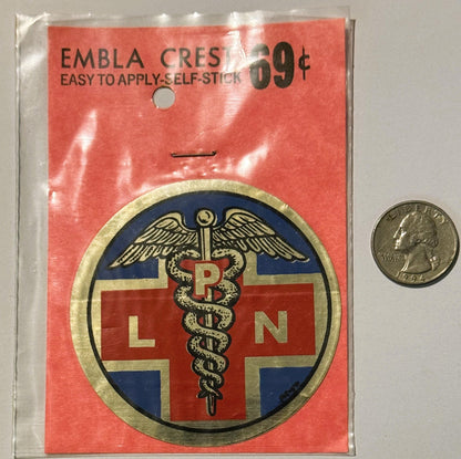 Vintage LPN emblem decal on red backing with quarter for scale, showing winged caduceus and cross design in blue and red.