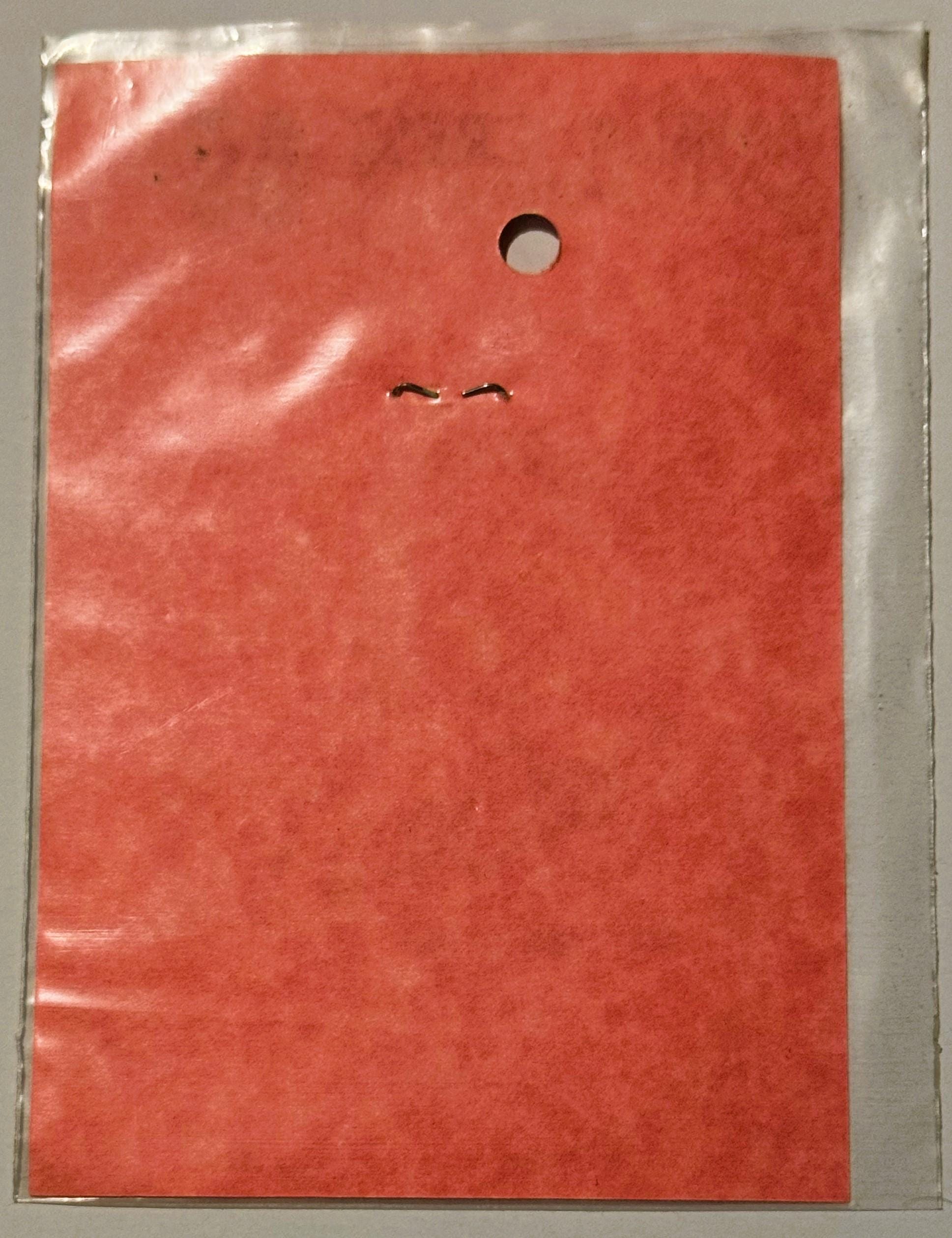 Coral-red rectangular decal in clear plastic sleeve with circular hole and two curved lines printed near center