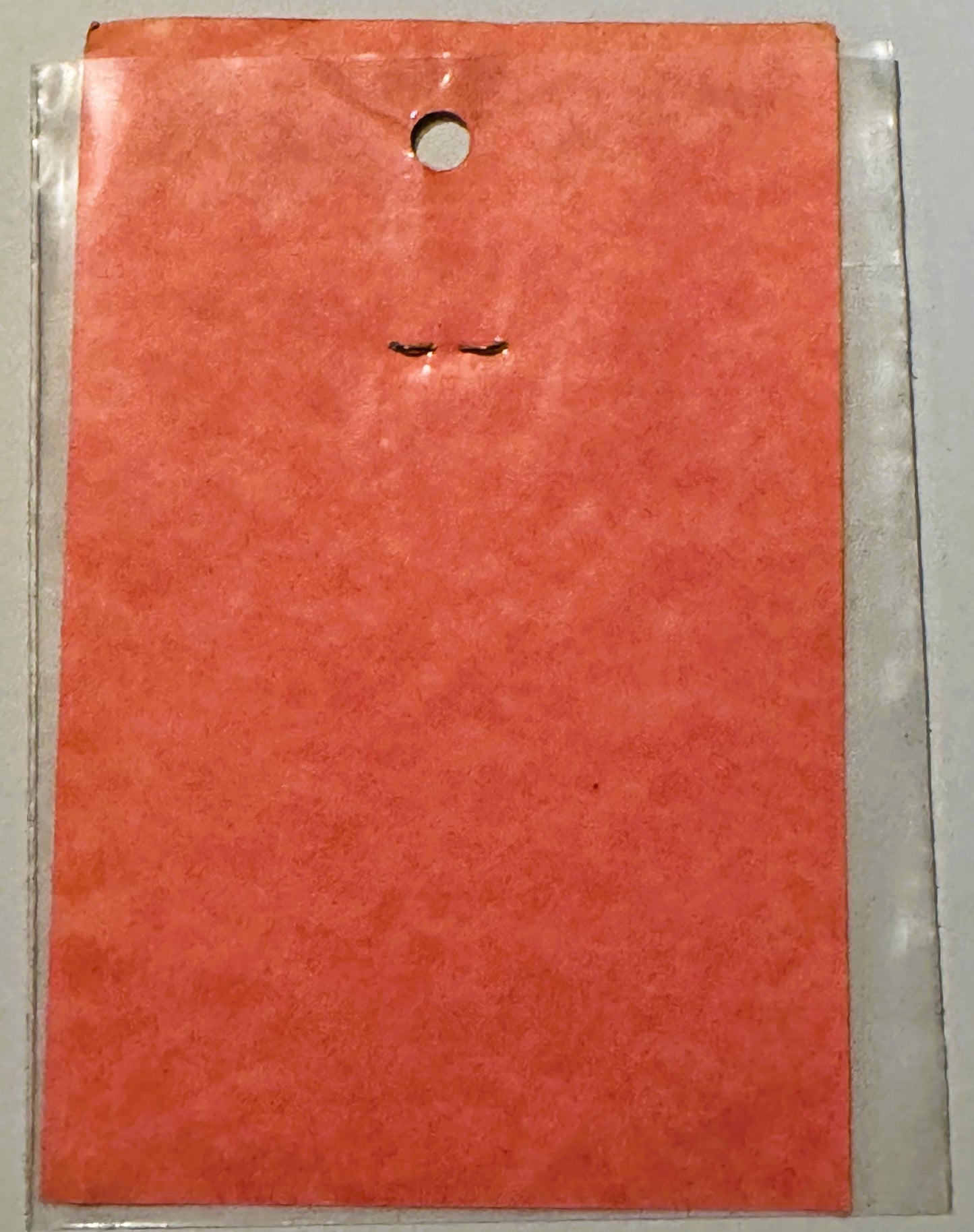 Coral-red vintage decal sticker in clear plastic package, showing minimalist closed eyes design, hung from hole at top