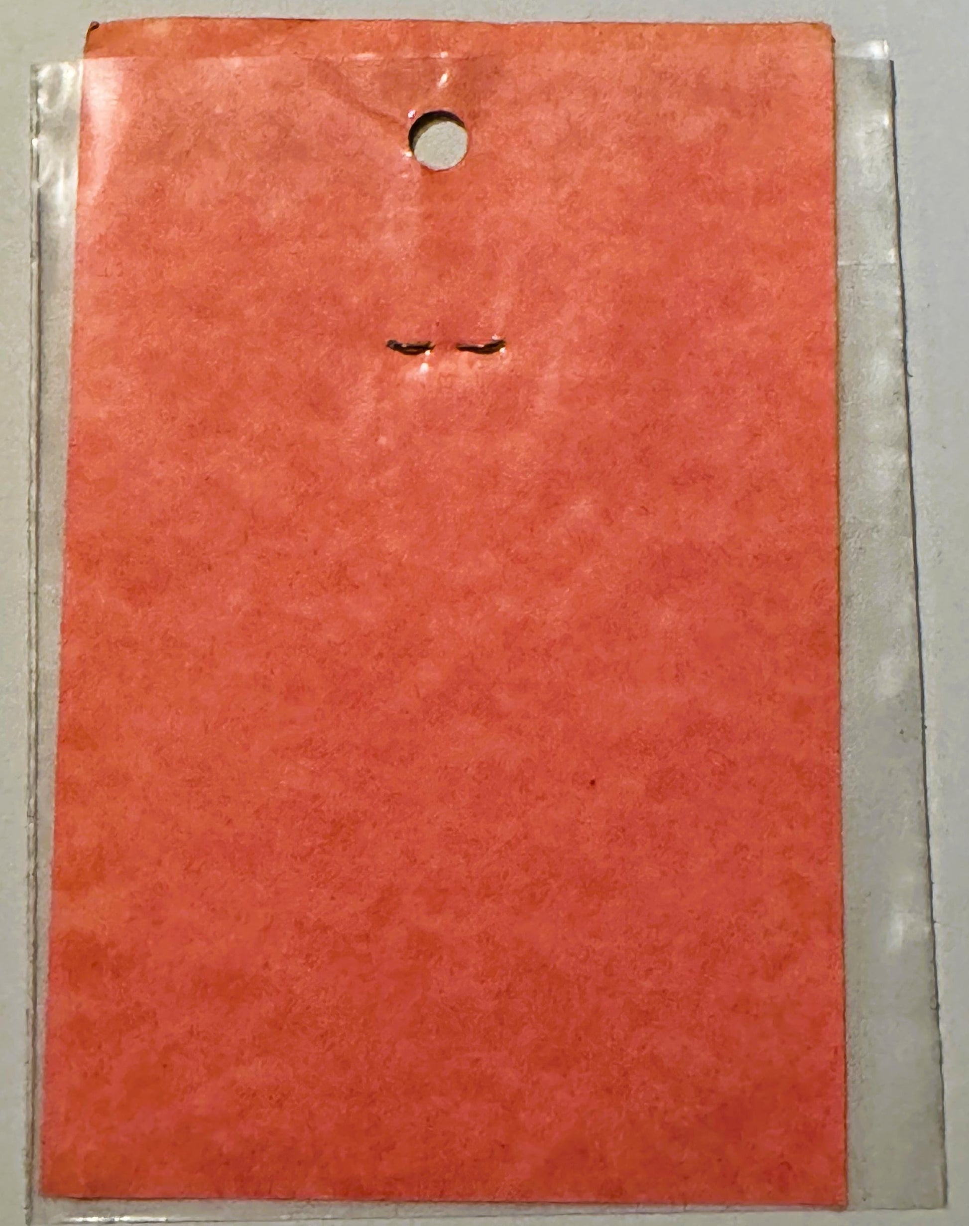 Coral-red vintage decal sticker in clear plastic package, showing minimalist closed eyes design, hung from hole at top