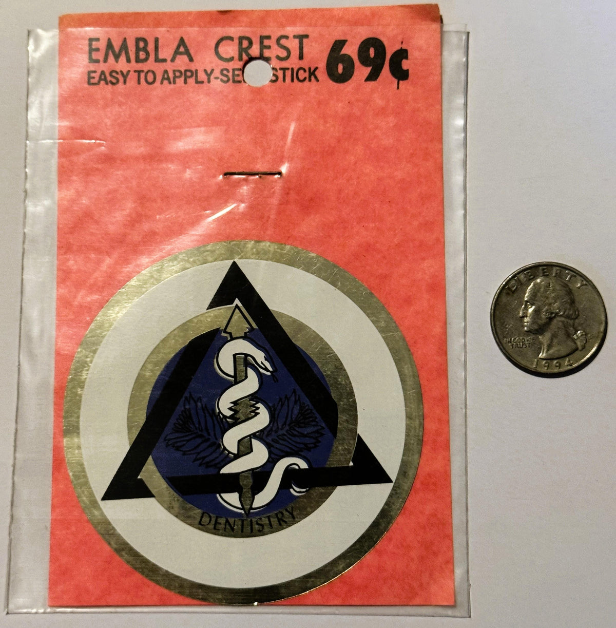 Vintage Embla Crest dental emblem decal on red packaging, priced 69¢, shown next to a quarter for scale.