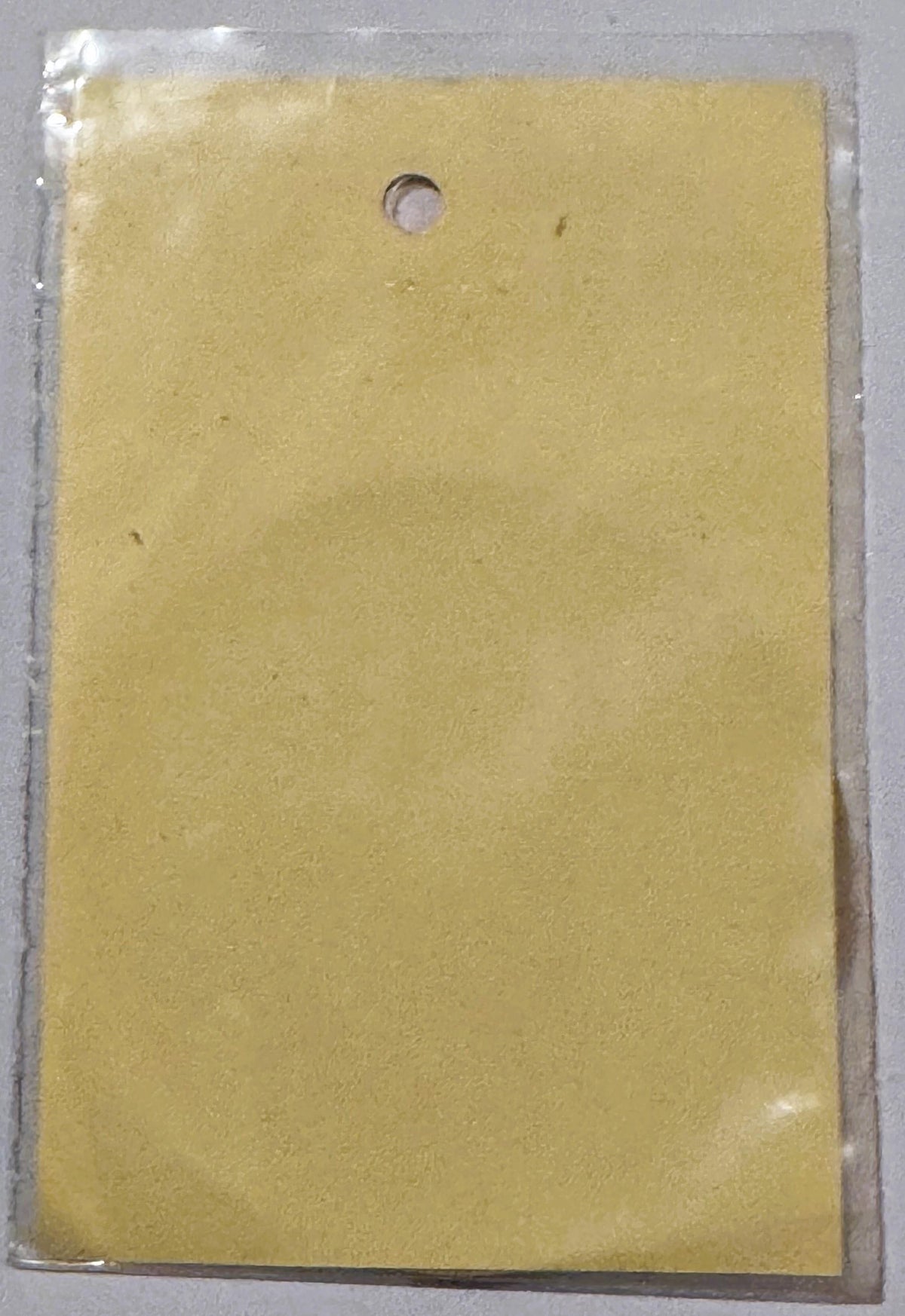Pale yellow vintage decal in clear plastic packaging with single hole punch at top, shown flat against gray surface