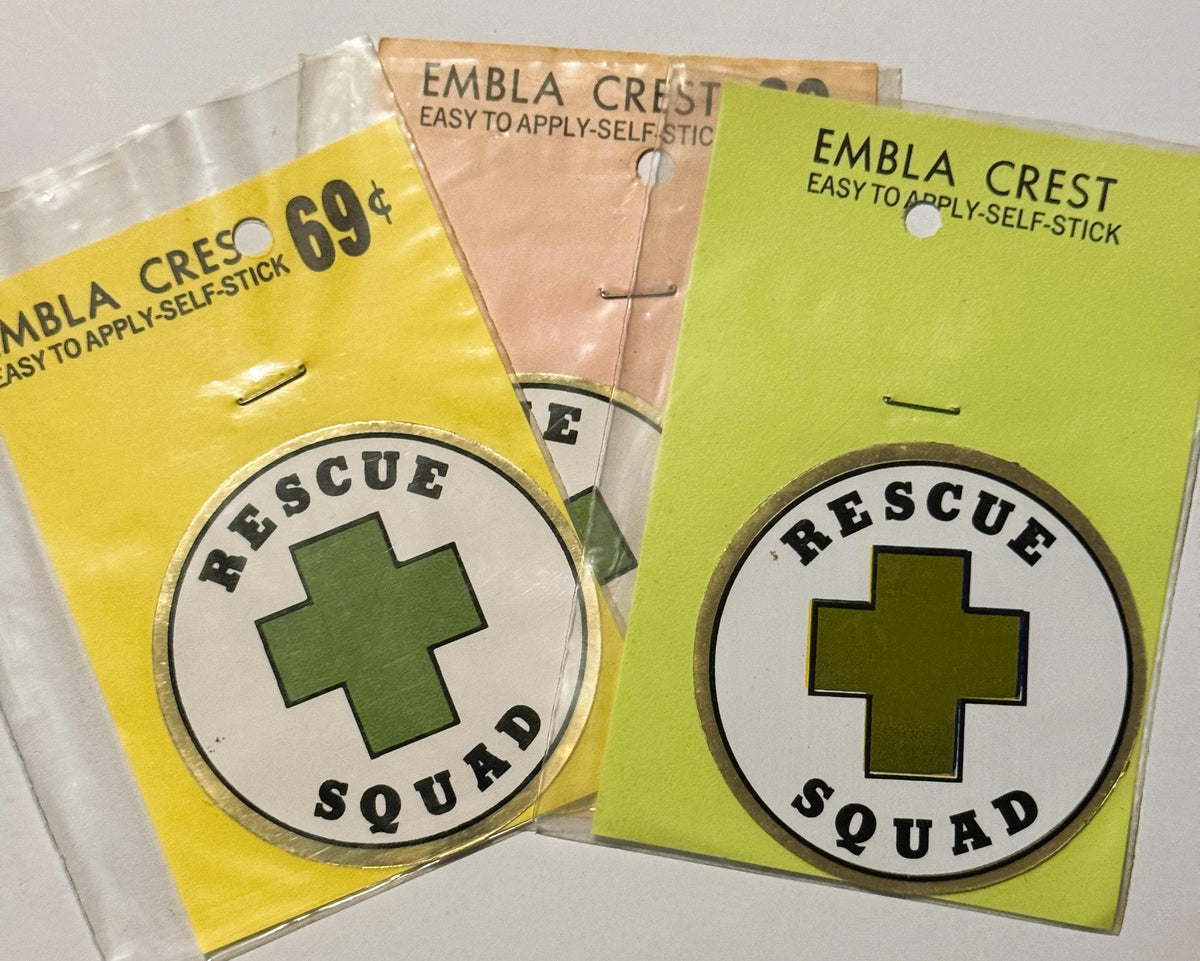 Three unopened vintage Embla Crest self-stick decals with green cross "Rescue Squad" emblems on yellow and lime backgrounds, 
