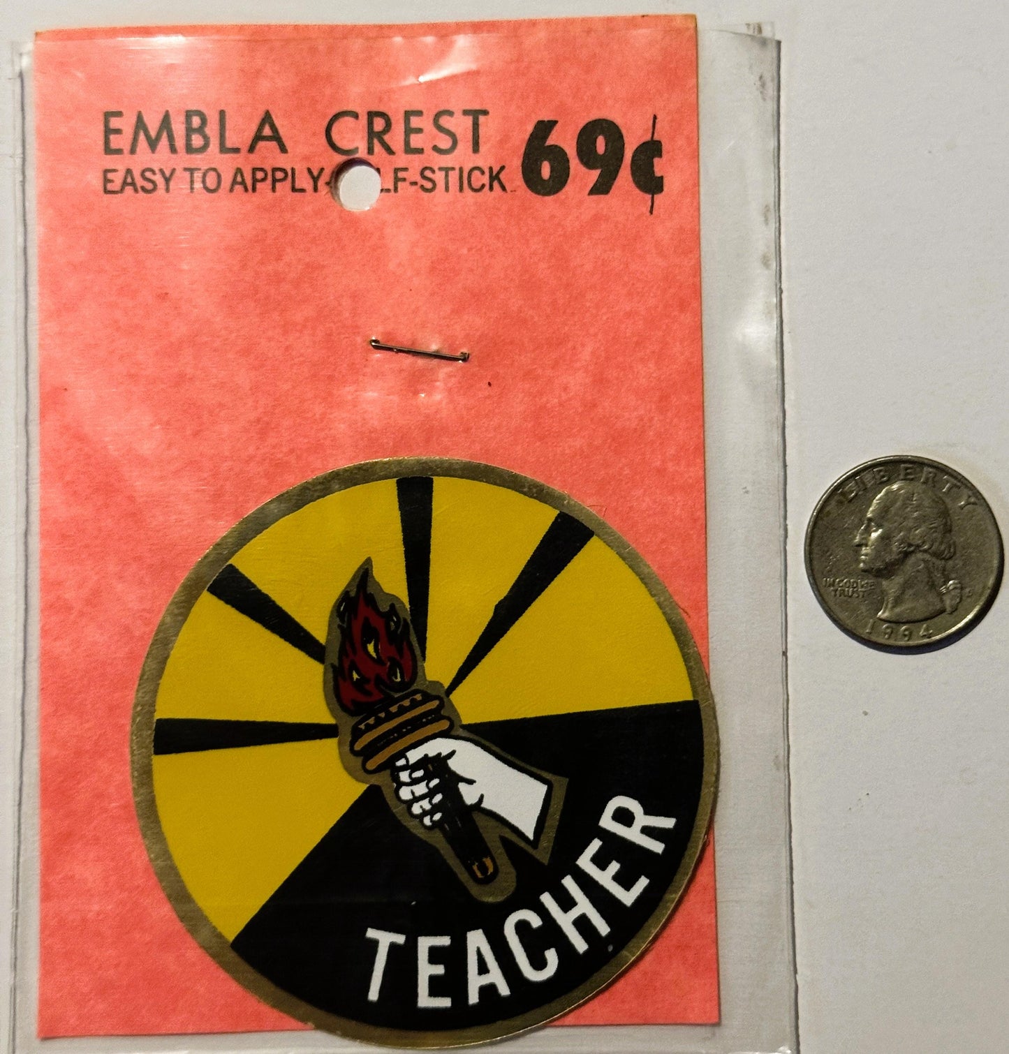 Vintage teacher decal on coral packaging showing torch emblem with yellow and black design, priced 69¢, displayed next to qua