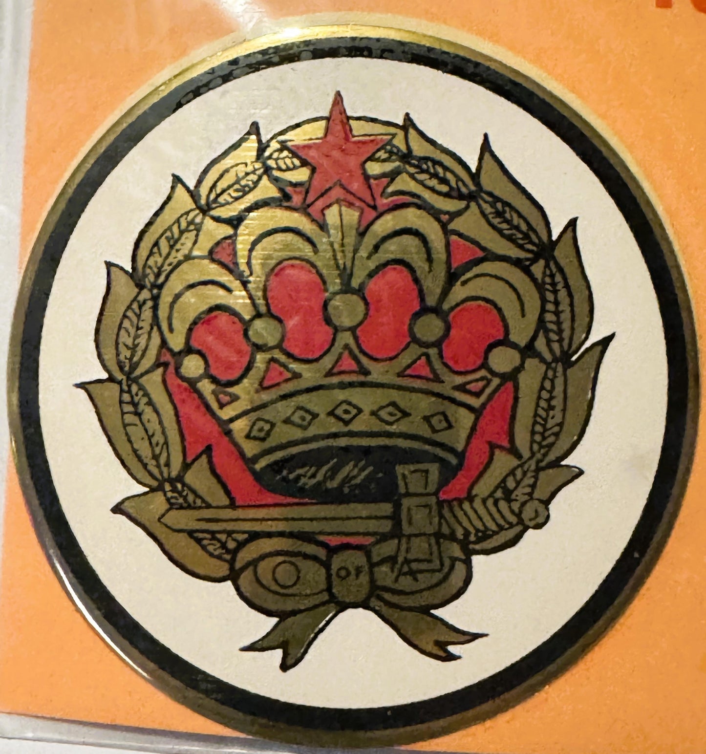 Circular decal featuring ornate gold crown with red jewels and star, surrounded by wheat laurels and ribbon bow, on cream bac