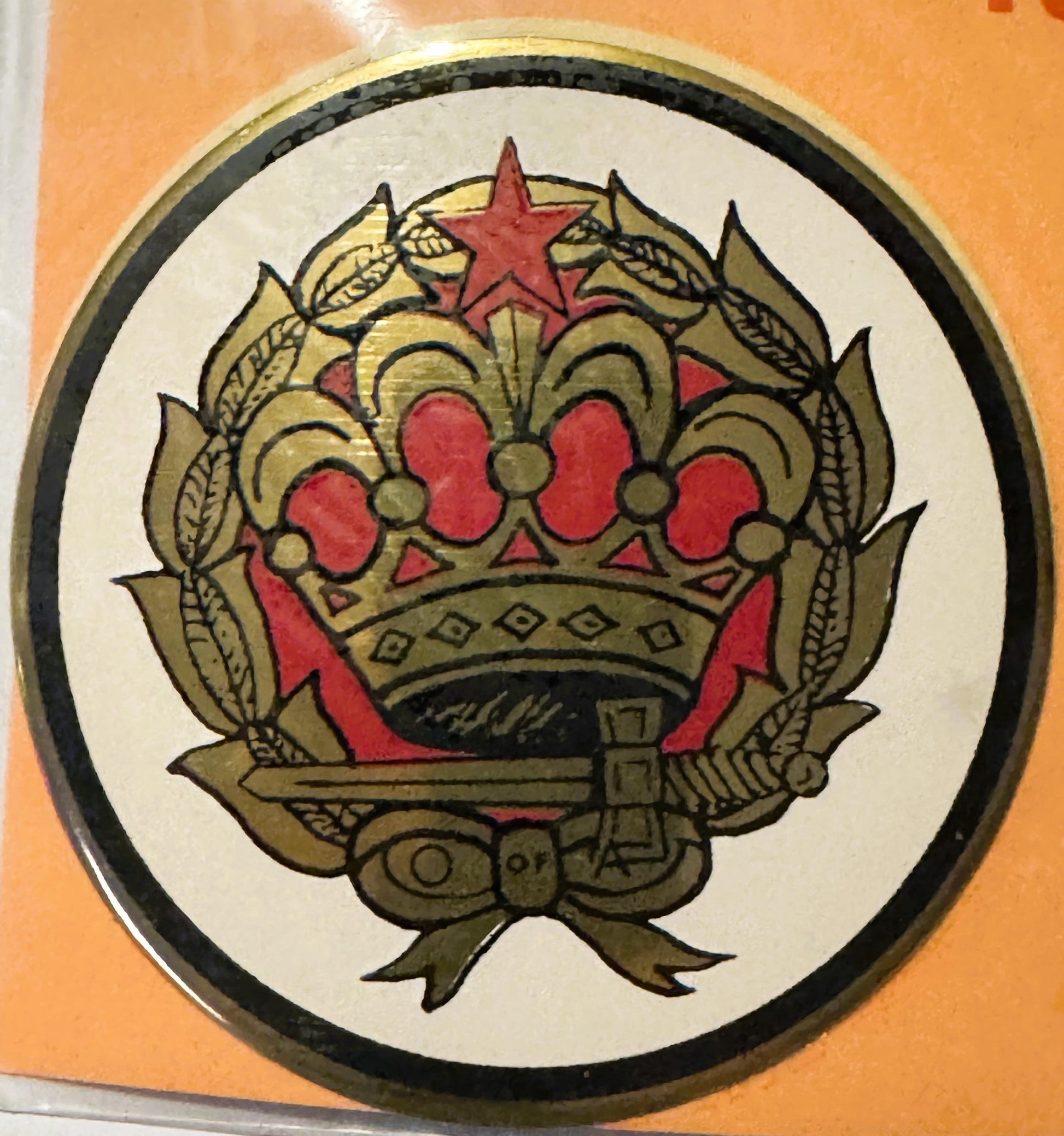 Circular decal featuring ornate gold crown with red jewels and star, surrounded by wheat laurels and ribbon bow, on cream bac