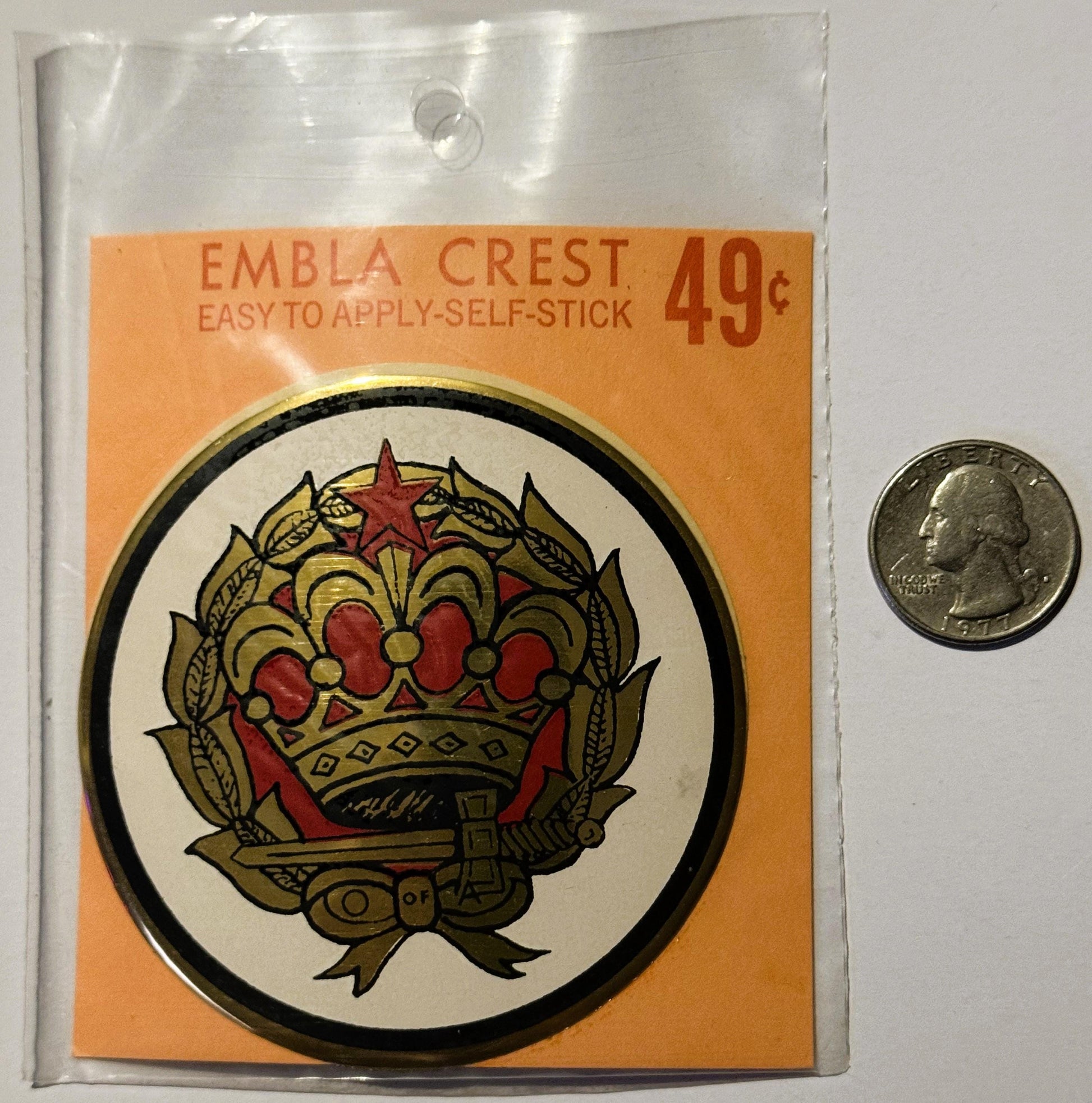 Vintage Embla Crest self-stick decal in unopened plastic package priced 49¢, shown next to quarter for scale