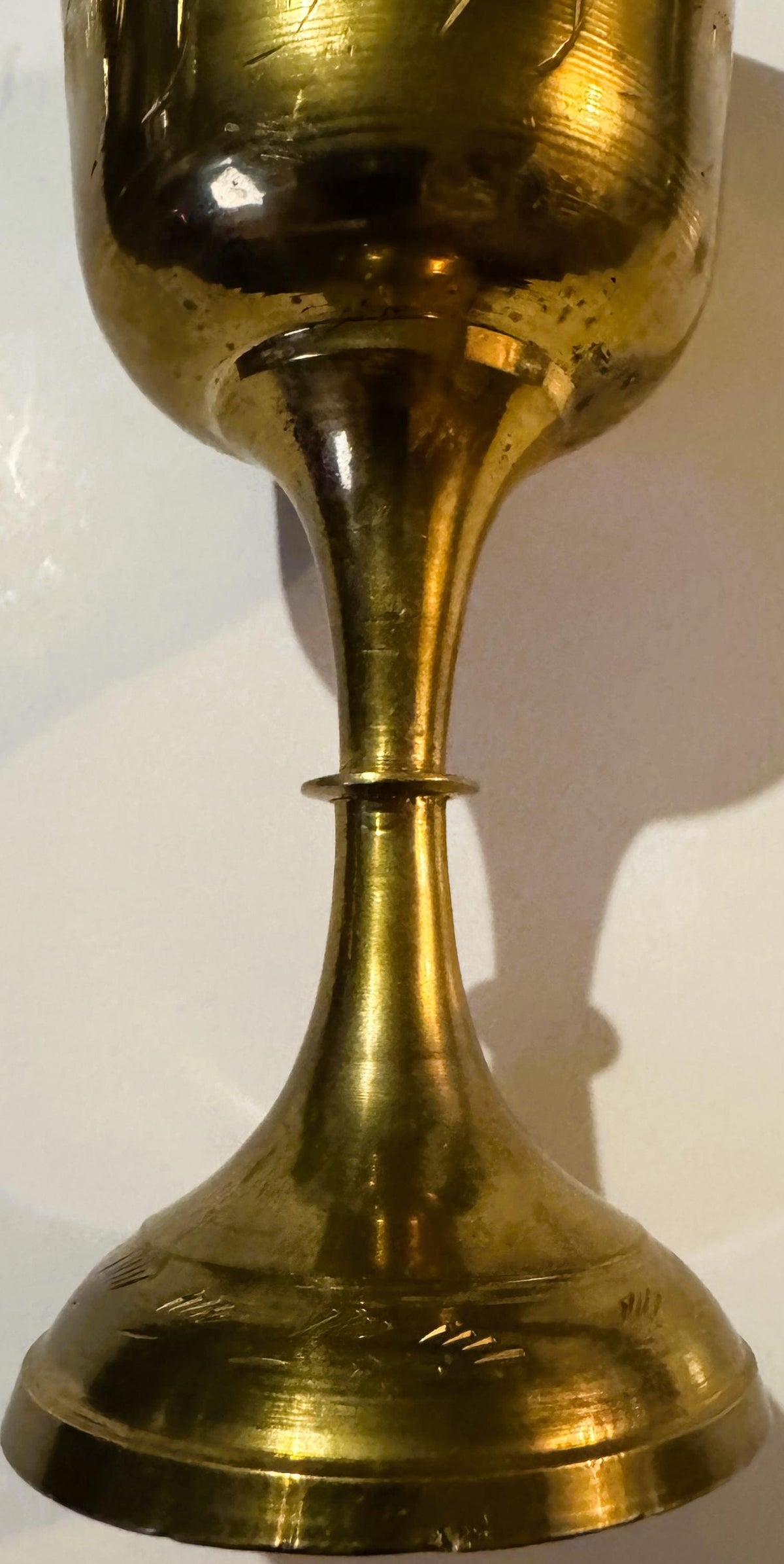 Vertical close-up of a brass goblet with etched bowl and tapered stem, showing bright cut engraving details and surface patin