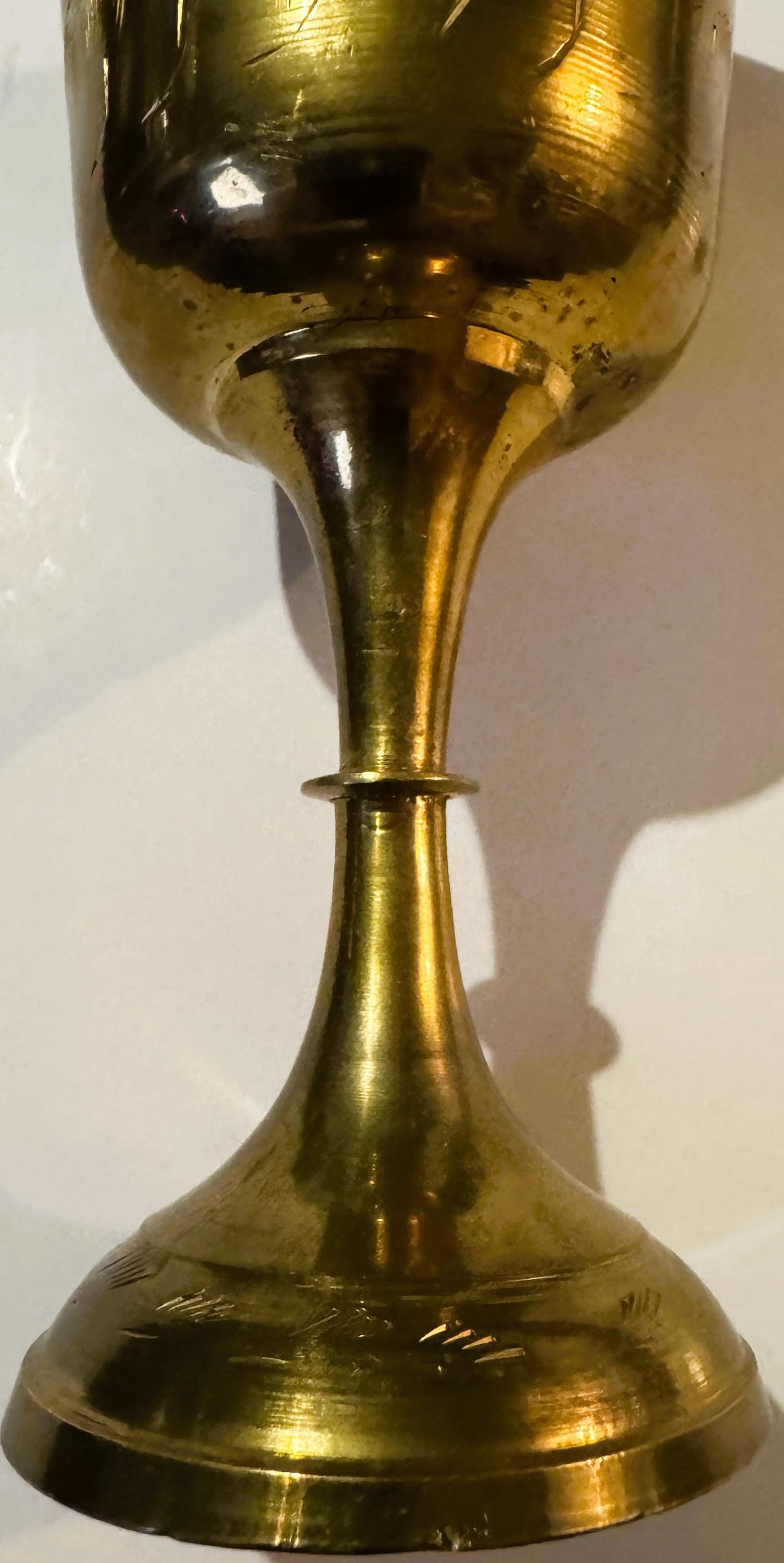 Vertical close-up of a brass goblet with etched bowl and tapered stem, showing bright cut engraving details and surface patin