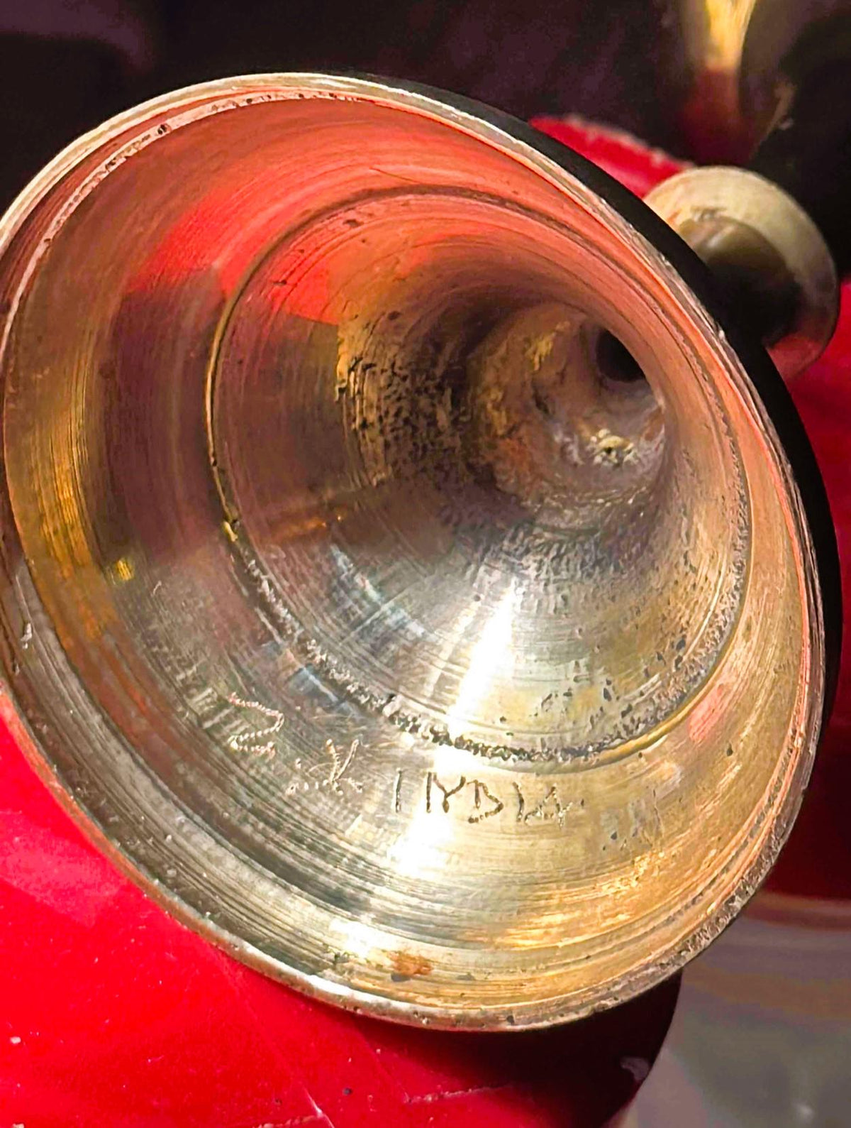 Close-up of brass goblet interior showing red-orange patina, bright-cut engraving, and wear marks, held against red fabric
