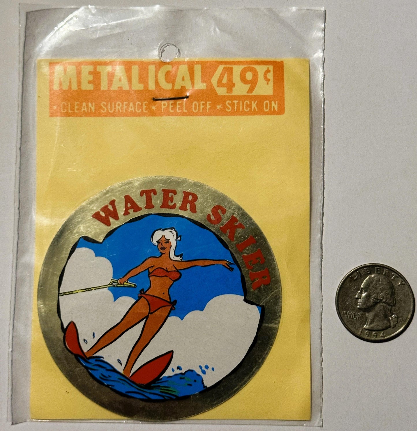 Vintage metallic water skier decal in plastic packaging with quarter for scale, showing woman in red bikini on blue backgroun