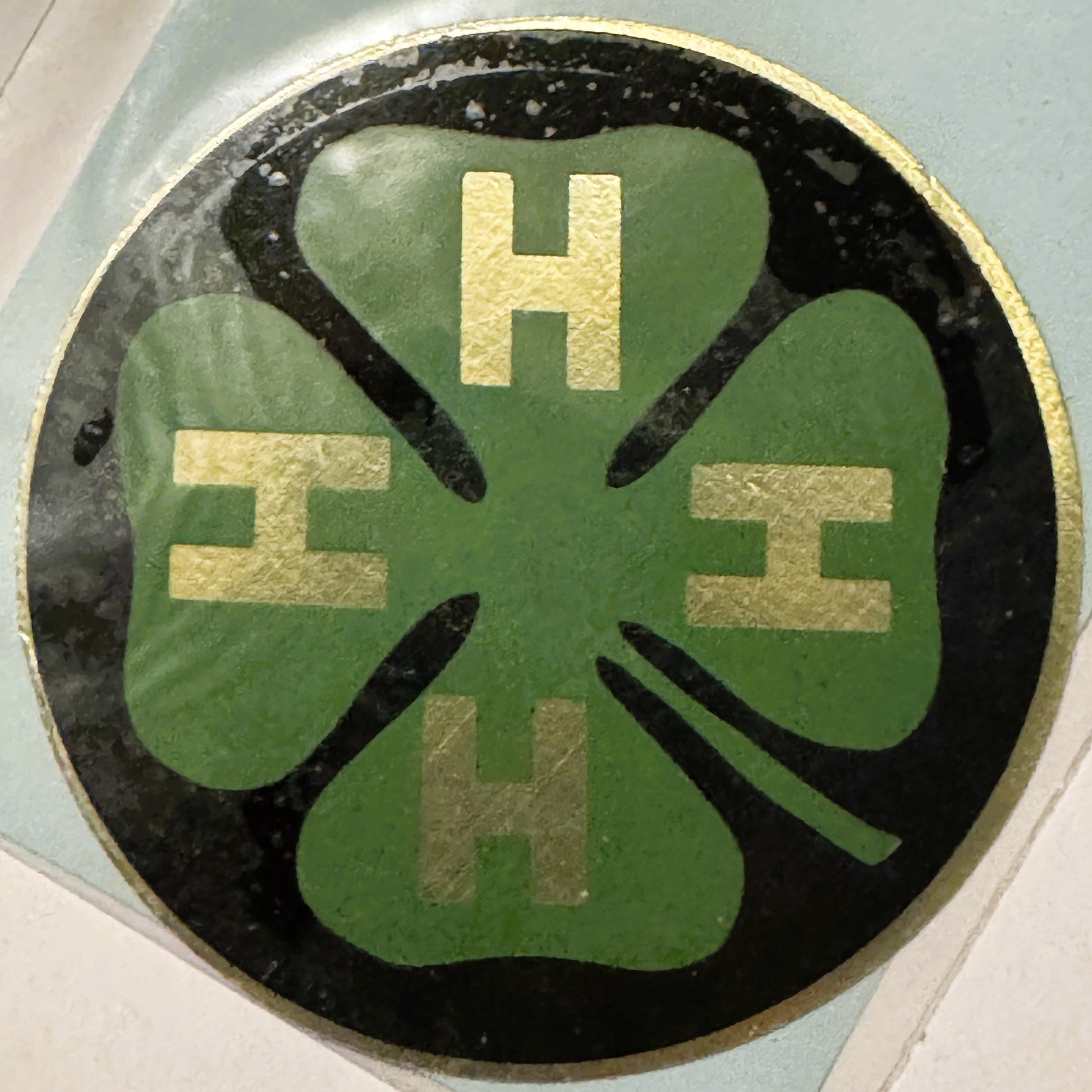 Circular green four-leaf clover decal with gold letter "H" at top and "4" repeated in corners on black background with gold r