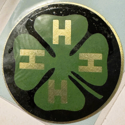 Circular green four-leaf clover decal with gold letter "H" at top and "4" repeated in corners on black background with gold r