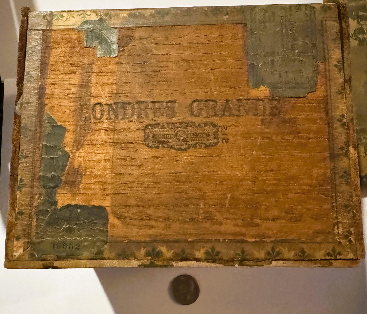 Weathered wooden cigar box with embossed text reading "RENTER'S GRANITE," metal corner brackets, and a coin placed below for 