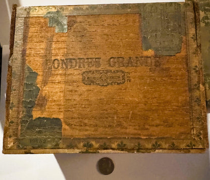 Weathered wooden cigar box with embossed text reading "RENTER'S GRANITE," metal corner brackets, and a coin placed below for 