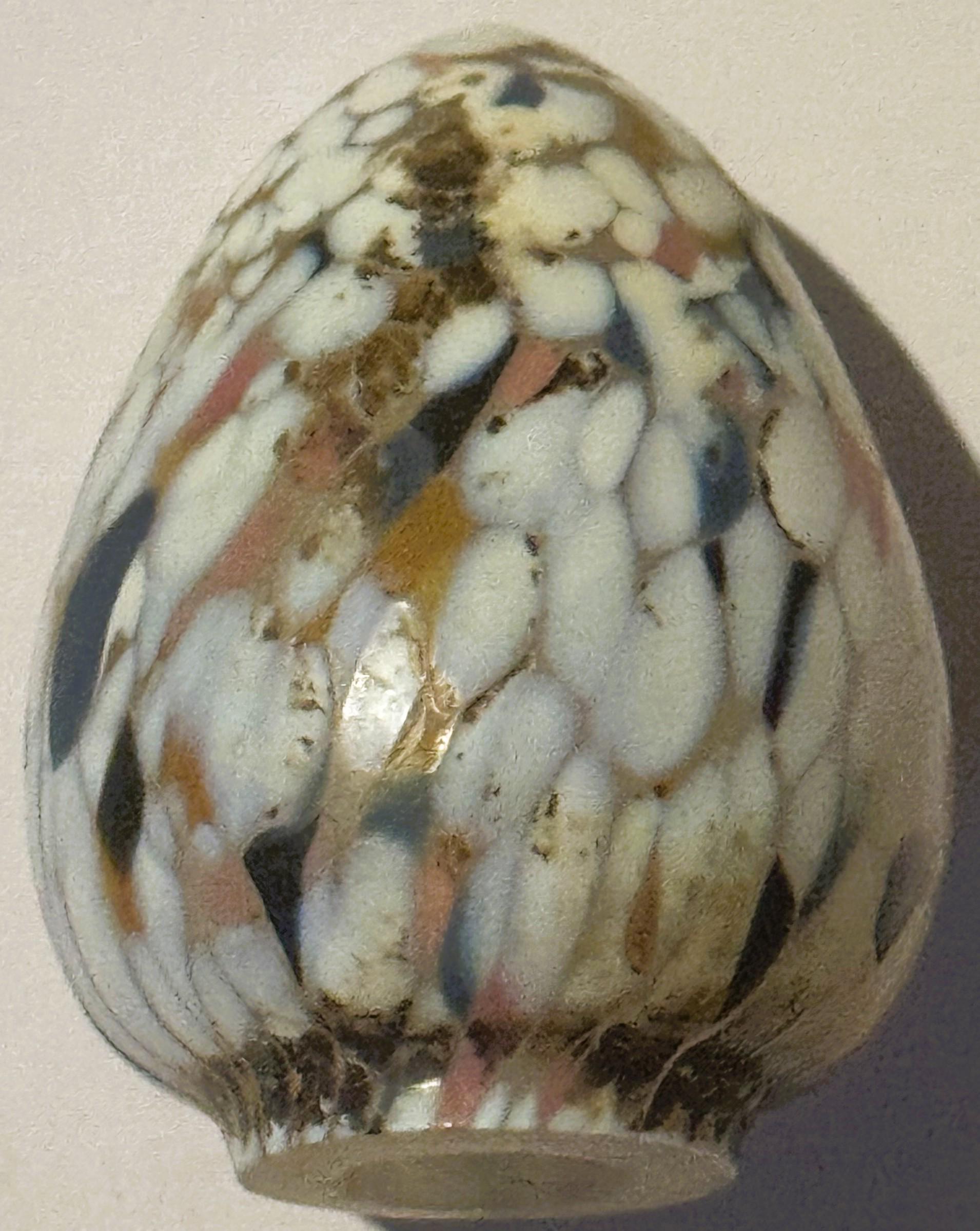 Egg-shaped art glass sculpture with white, cream, brown and rust spatter pattern, shown from front against neutral background