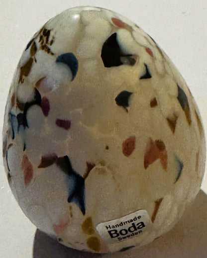 Cream-colored art glass egg with colorful confetti specks in blue, red, and brown, displaying cutout windows, labeled "Handma