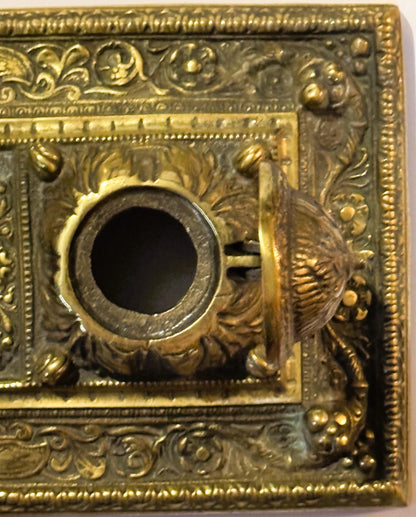 Close-up of the right well's hinge on the brass double inkstand, lid raised upright and stopping short of flat