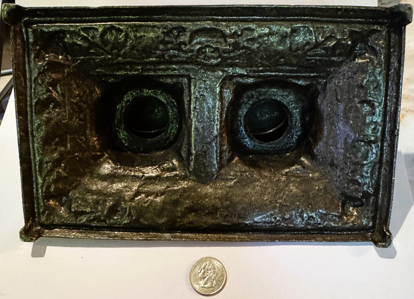 Underside of the brass double inkstand, raw unfinished metal with green verdigris patina across the reverse