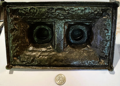 Underside of the brass double inkstand, raw unfinished metal with green verdigris patina across the reverse