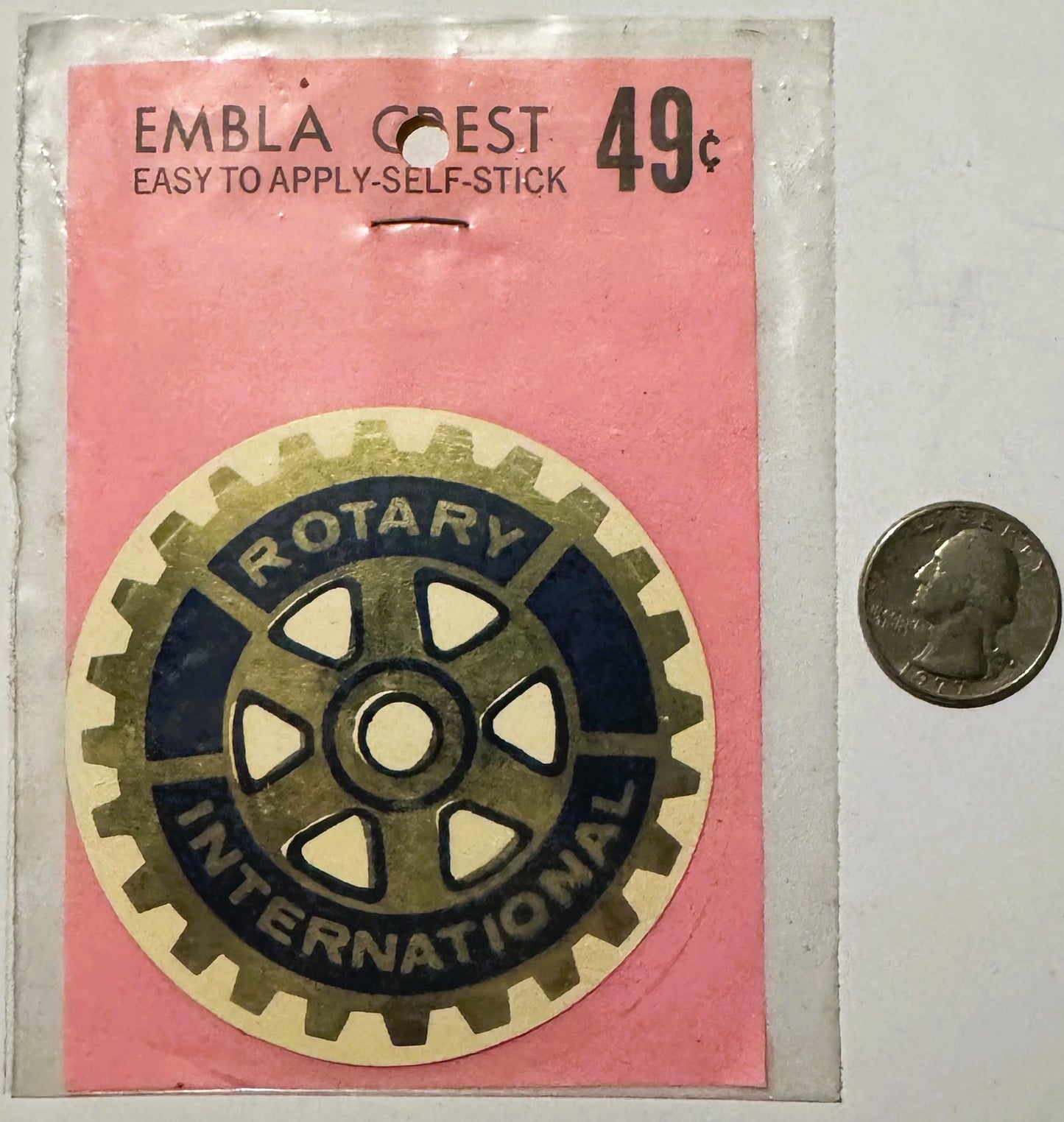 Vintage Rotary International self-stick emblem on pink backing with gear logo, priced 49¢, shown next to coin for scale