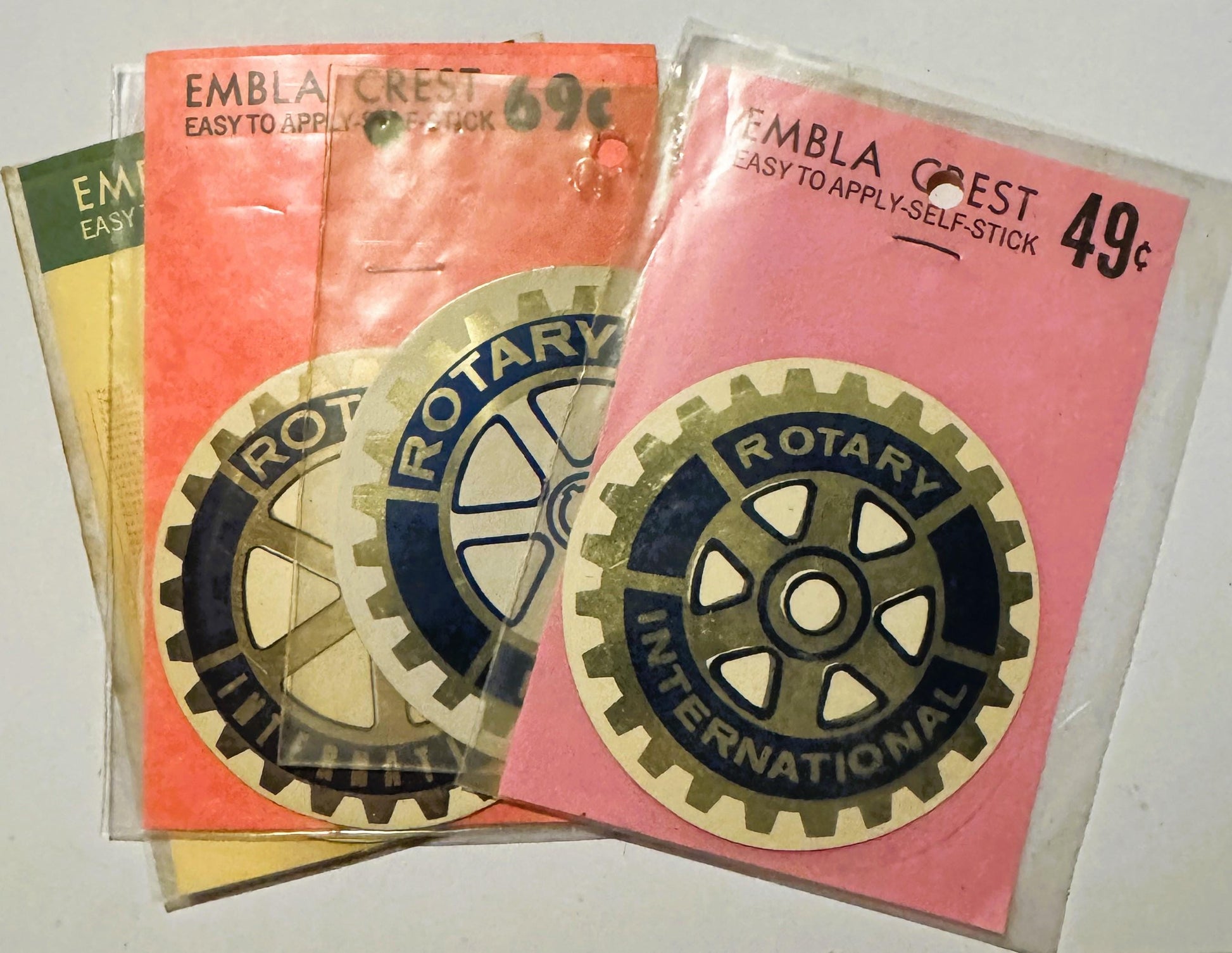 Three vintage Rotary International Embla Crest self-stick decals in orange, pink, and yellow packaging priced at 49 cents, di