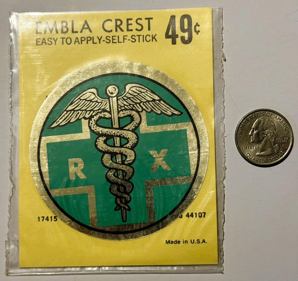 Vintage pharmacy Rx emblem sticker on yellow backing with green medical caduceus symbol, next to quarter coin for scale