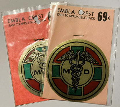 Two vintage self-stick medical decals in original packaging: coral-colored and tan, each featuring an MD caduceus emblem with