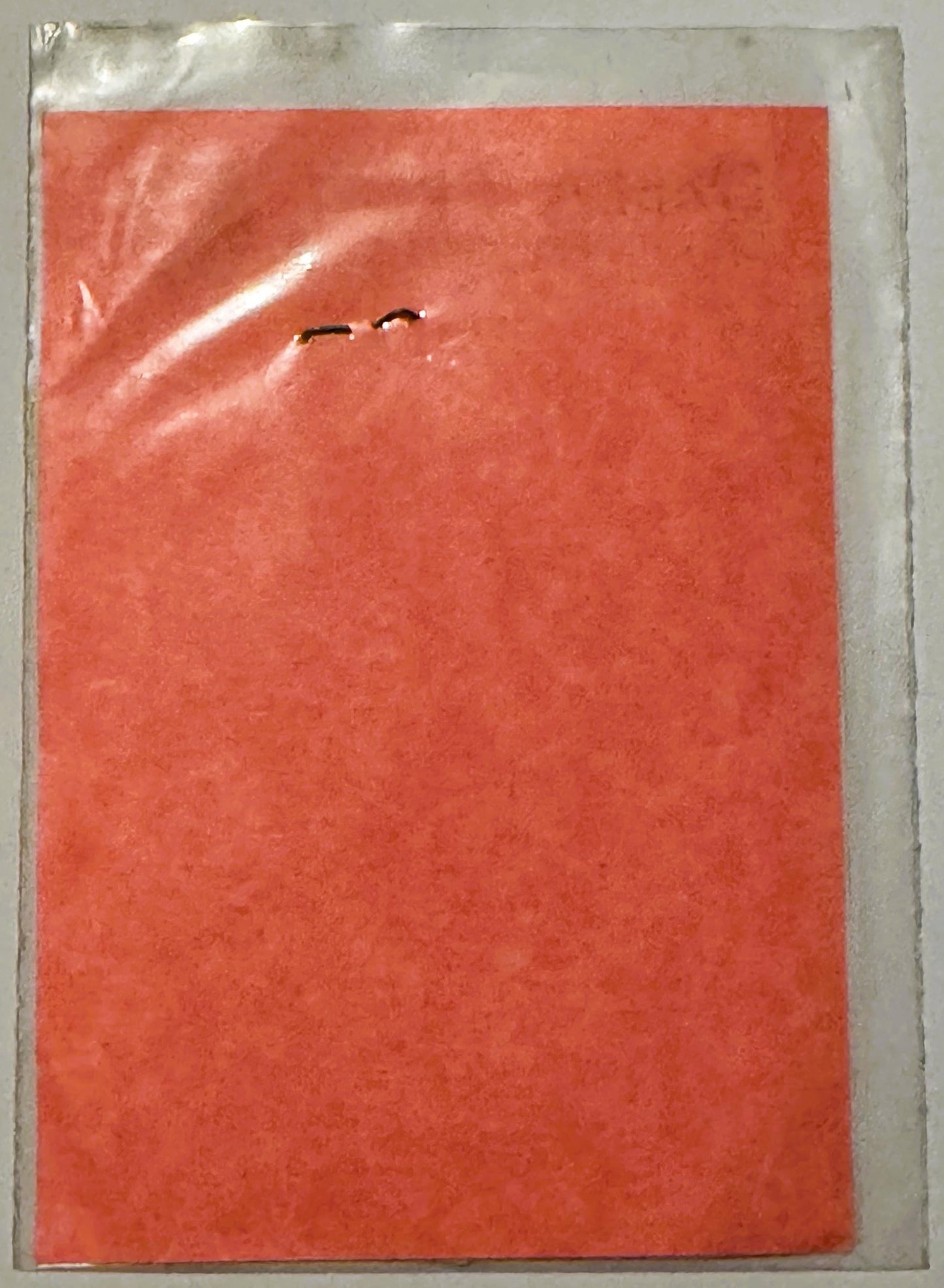Vintage red decal sticker in clear plastic packaging, showing small dark emblem or text mark in upper center area