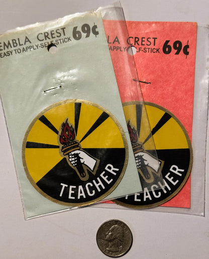 Two vintage teacher decals in original packaging showing torch emblem with yellow and black rays, priced at 69 cents, display