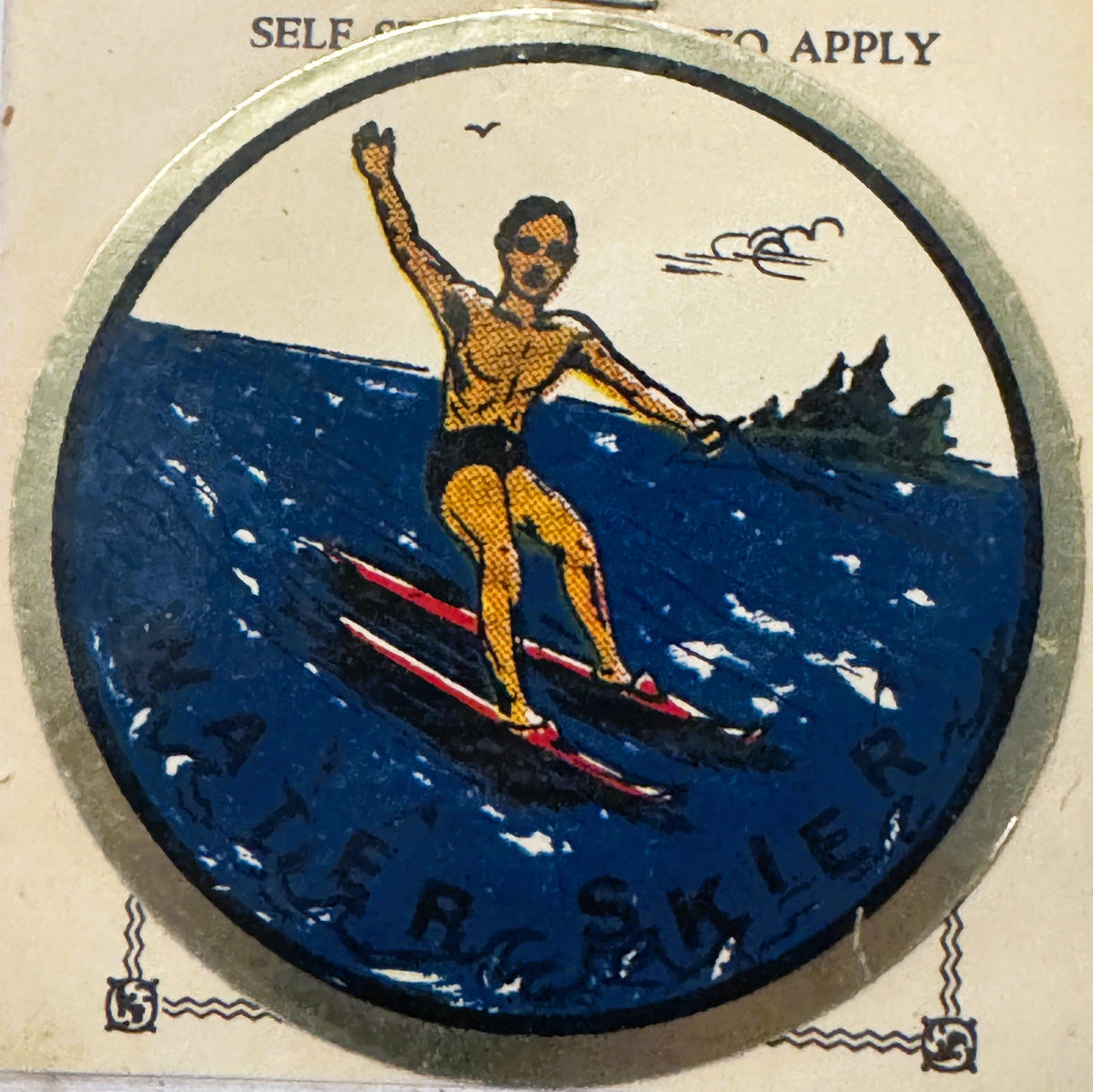 Circular vintage water skier decal showing a muscular figure in yellow swimsuit on red skis, fist raised, against deep blue w