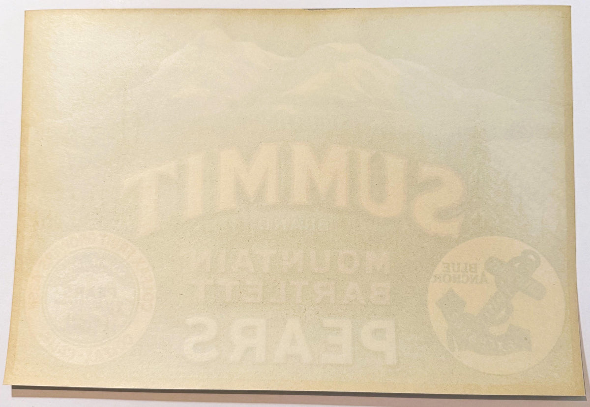 Cream-colored vintage fruit crate label with faint embossed text and circular logos visible at left and right edges, photogra