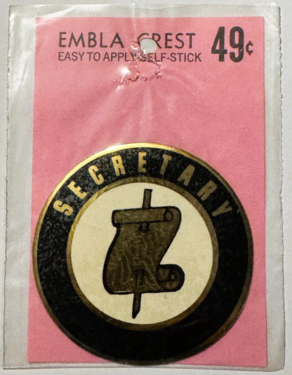 Unopened vintage self-stick emblem crest decal on pink card stock priced at 49 cents, featuring circular black and cream seal