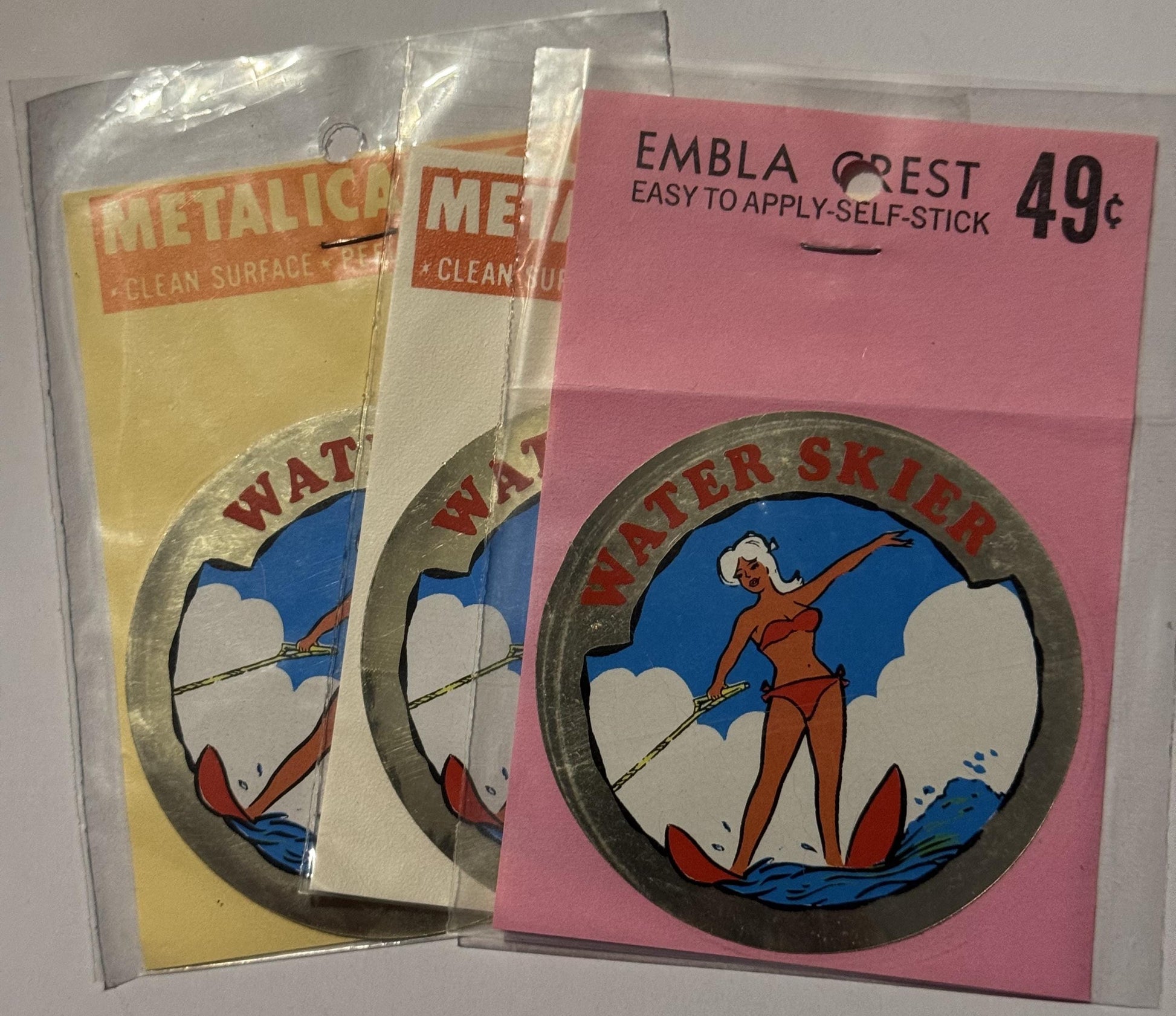 Vintage water skier decals in clear packaging: two rectangular "Metallic" packets with yellow/cream backgrounds and one circu