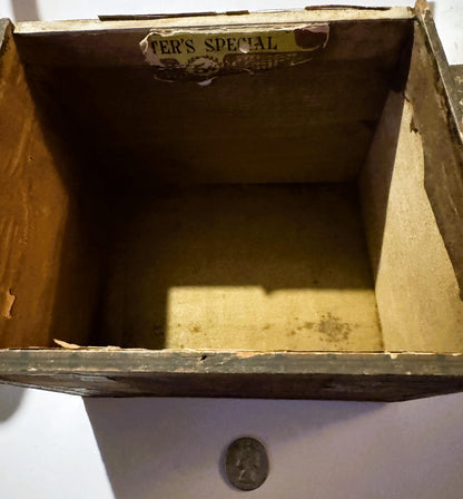 Empty wooden cigar box with "Renter's Special" label visible on lid, shown open from above with a quarter for scale