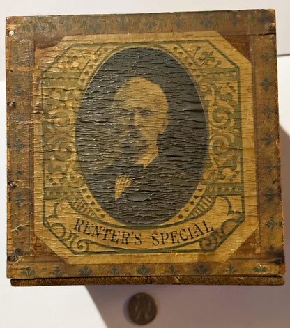 Weathered wooden cigar box with embossed gold frame around central oval portrait, "RENTER'S SPECIAL" text visible below, coin