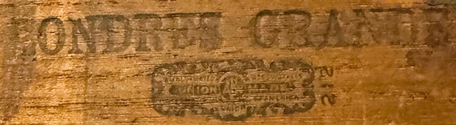 Close-up of embossed wooden cigar box lid showing faded text and decorative brand label in tan and brown tones