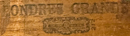 Close-up of embossed wooden cigar box lid showing faded text and decorative brand label in tan and brown tones