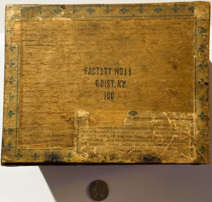 Aged wooden cigar box lid with decorative fleur-de-lis border, stamped "Factory No. 11, 6 Dist. KY, 100," penny shown for sca