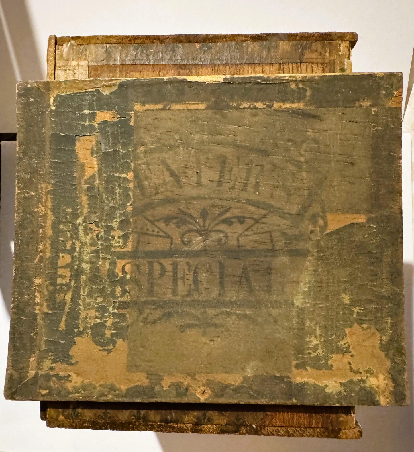Weathered cigar box lid with faded green and gold paint, ornate decorative border, partially illegible embossed text and eagl