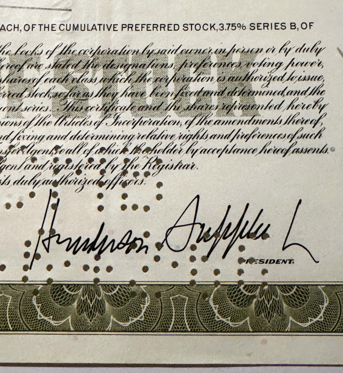 Close-up of signed stock certificate showing cursive signature and "PRESIDENT" label, with decorative border and ornate patte