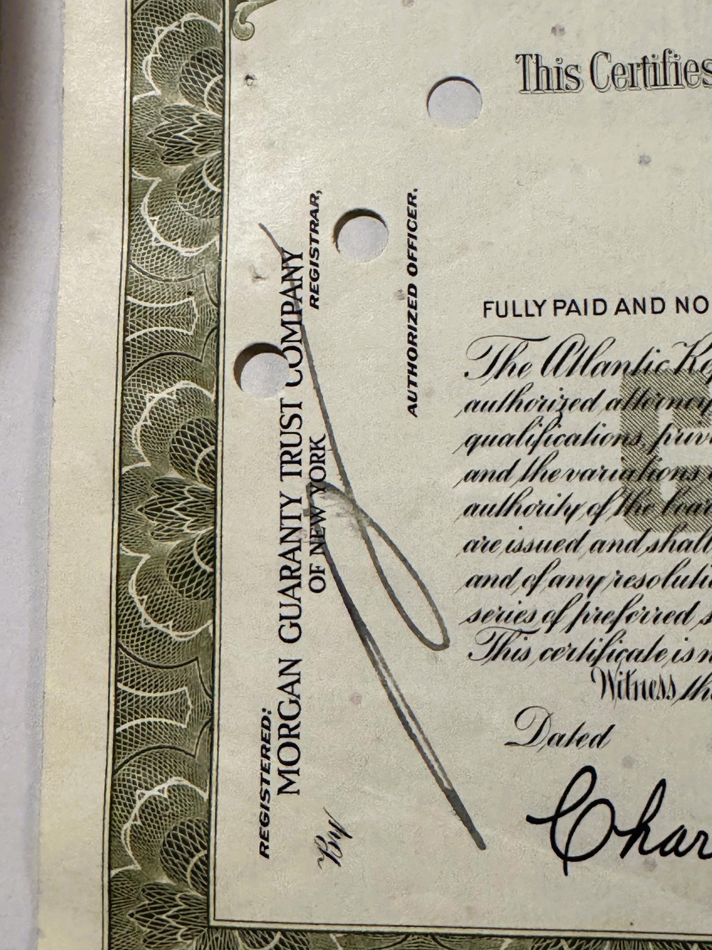 Close-up of vintage stock certificate with ornate border, showing "Morgan Guaranty Trust Company" text, punch holes, handwrit